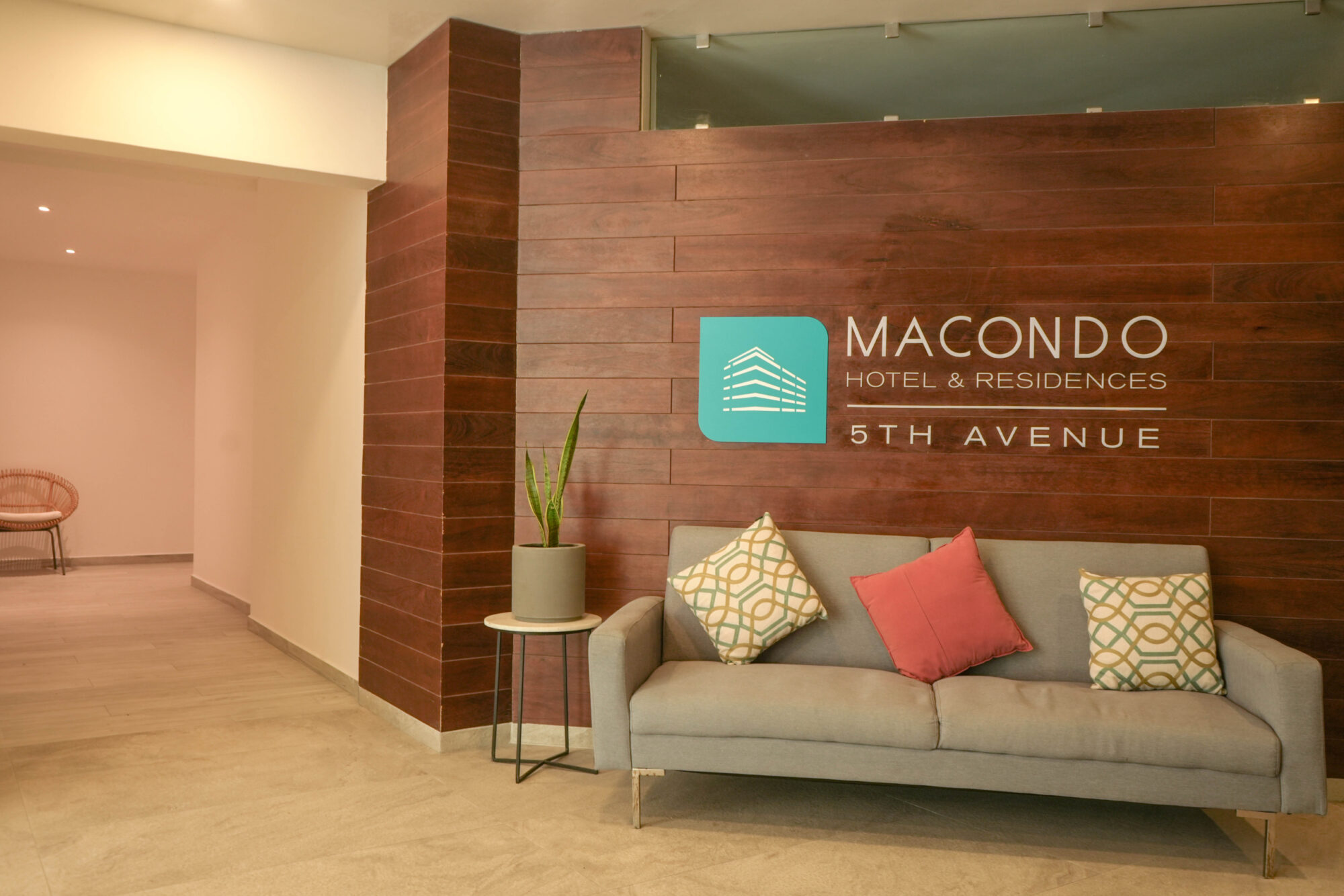 Lobby moderno de Macondo Hotel & Residences 5th Avenue, con pared de madera, decoración minimalista y ambiente acogedor, dentro de un desarrollo con departamentos en venta en Playa del Carmen que combina lujo, confort y hospitalidad de alto nivel.