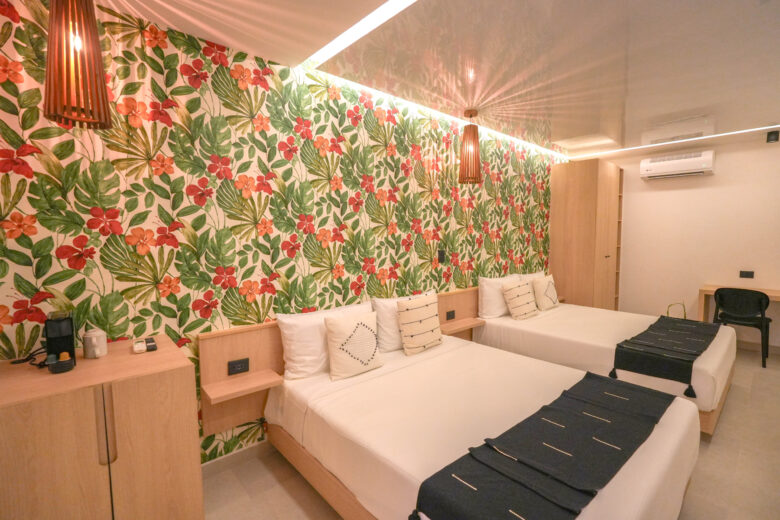 Habitación doble de estilo tropical con diseño contemporáneo, papel tapiz de hojas y flores, iluminación cálida y detalles naturales, dentro de un desarrollo residencial de lujo con departamentos en venta en Playa del Carmen, pensado para disfrutar el confort y la esencia del Caribe.