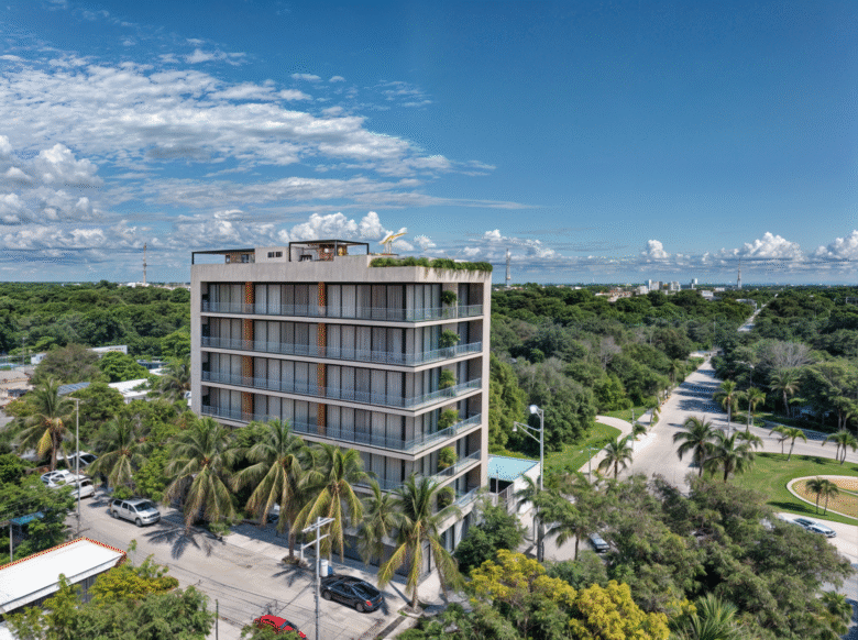 Vista aérea del edificio Macondo Punta Esmeralda, un desarrollo con departamentos en venta en Playa del Carmen, rodeado de vegetación tropical y palmeras, con fachada moderna, amplios ventanales y rooftop con áreas sociales.