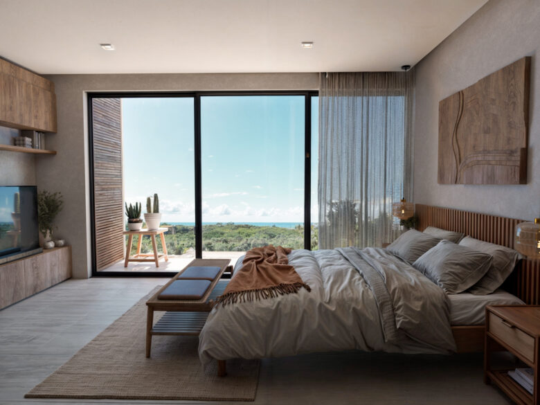 Habitación del desarrollo Macondo Punta Esmeralda con cama matrimonial, decoración en tonos neutros, muebles de madera, ventanal panorámico con vista al mar Caribe y vegetación tropical, dentro de los departamentos en venta en Playa del Carmen.
