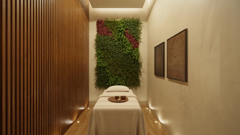 Sala de masajes del spa en Macondo Tulum con iluminación cálida, muro verde natural y acabados en madera, diseñada para el bienestar dentro de los departamentos en venta en Tulum.