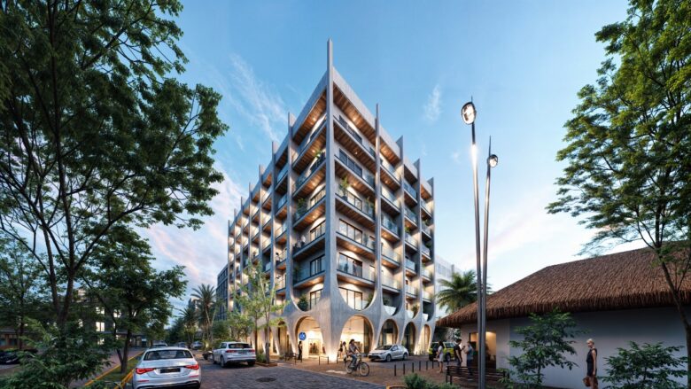 Vista exterior del edificio Macondo Corazón en Playa del Carmen, con fachada moderna de concreto y arcos escultóricos, balcones con barandales de cristal, iluminación cálida y entorno urbano rodeado de vegetación tropical, automóviles y peatones. Un desarrollo con departamentos en venta en Playa del Carmen, ubicado sobre la emblemática Calle Corazón.