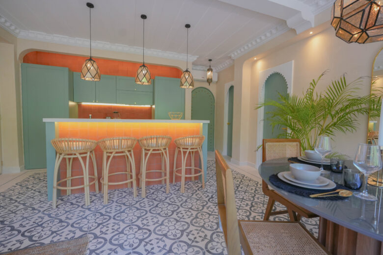 Cocina y barra desayunador en una unidad de Pink Riad Tulum, con azulejos en tonos terracota, gabinetes verde menta y lámparas de hierro forjado con diseños geométricos. Detalle distintivo de los departamentos en venta en Tulum.
